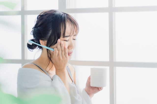 歯がしみて頬をおさえている女性の写真